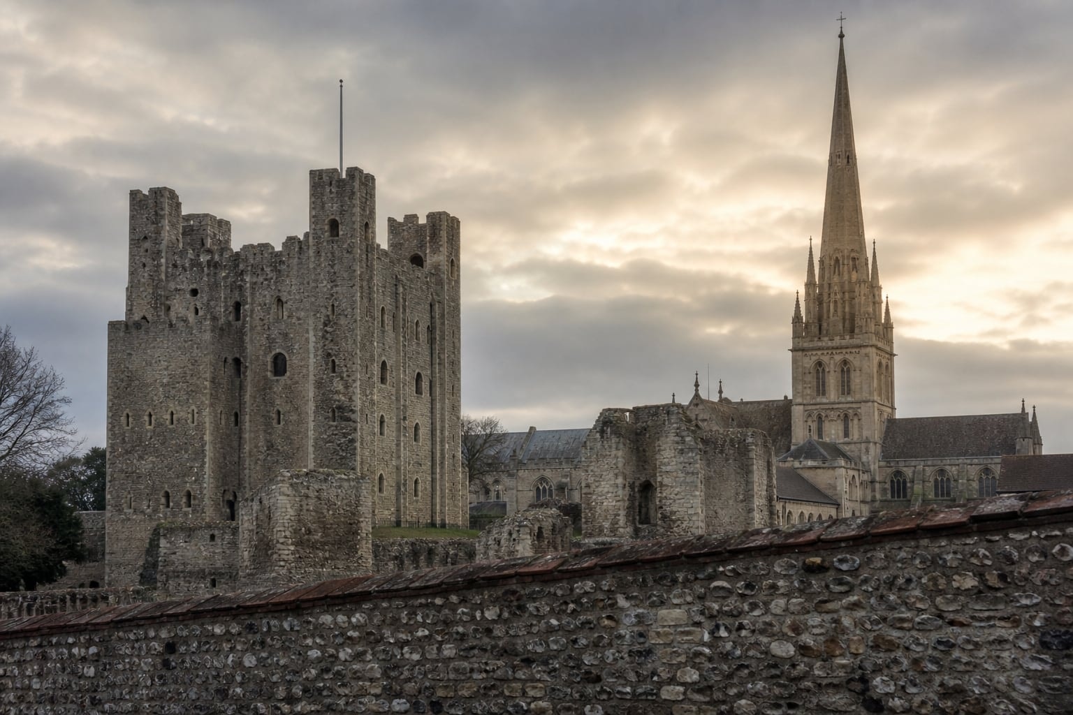 Weathered stone keep and cathedral spire seen across a quiet close